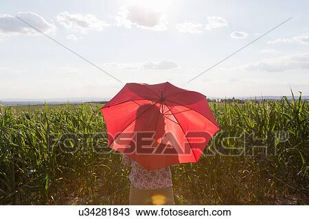 Stock Image - Woman standing holding red umbrella. Fotosearch