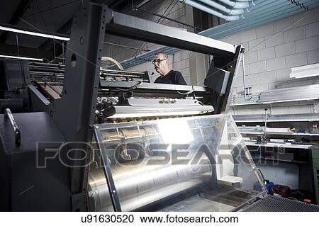 Stock Image - Worker operating printing machine in print workshop. Fotosearch