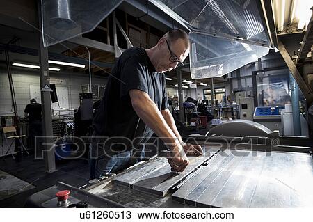 Stock Image - Worker servicing print machine in printing workshop. Fotosearch
