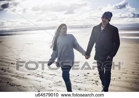 Stock Image - Young couple holding hands, Brean Sands, Somerset, England. Fotosearch