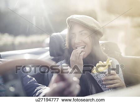 Young couple in convertible, woman eating chips View Large Photo Image Stock Photo - Young couple in convertible, woman eating chips. Fotosearch