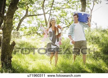 Stock Image - Young couple in forest with bunting and cool box. Fotosearch