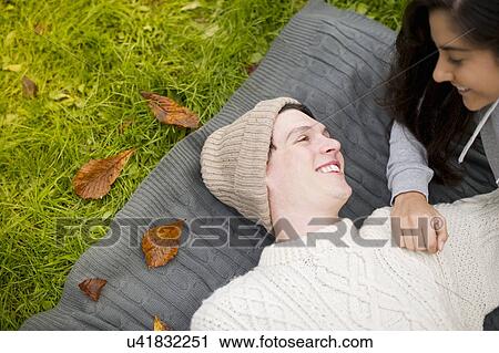 Stock Image - Young couple lying on rug, man wearing knit hat. Fotosearch