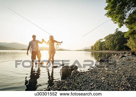 Stock Image - Young couple paddling in lake, Cumbria, England, UK. Fotosearch