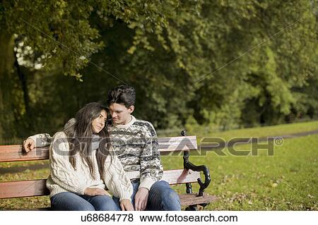 Young couple sitting on park bench View Large Photo Image Stock Photo - Young couple sitting on park bench. Fotosearch