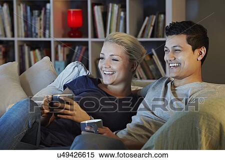 Young couple sitting on sofa with hot drinks, watching tv View Large Photo Image Stock Photography - Young couple sitting on sofa with hot drinks, watching tv. Fotosearch