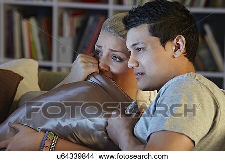 Young couple watching horror movie, hiding behind cushion View Large Photo Image Picture - Young couple watching horror movie, hiding behind cushion. Fotosearch