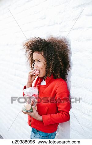 Stock Photograph - Young girl leaning against wall eating macaroons. Fotosearch