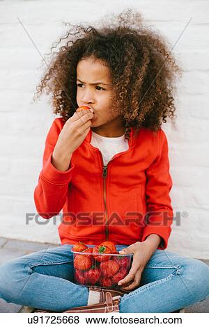 Stock Photo - Young girl sitting cross legged eating strawberries. Fotosearch
