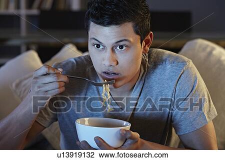 Young man eating noodles and watching tv View Large Photo Image Stock Image - Young man eating noodles and watching tv. Fotosearch