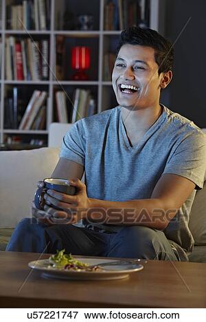 Young man laughing at television View Large Photo Image Stock Photo - Young man laughing at television. Fotosearch