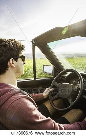 Stock Photograph - Young man leaning driving convertible. Fotosearch