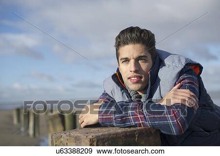 Stock Photo - Young man leaning on groyne, Brean Sands, Somerset, England. Fotosearch