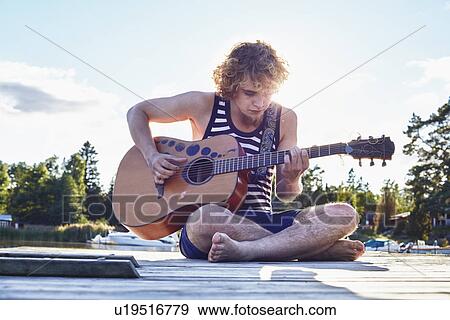 Stock Photo - Young man playing guitar on pier, Gavle, Sweden. Fotosearch