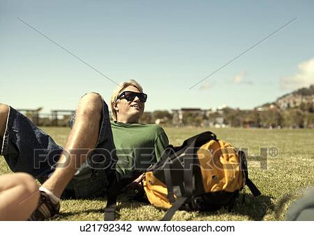 Stock Image - Young man reclining in park with backpack, Cape Town, South Africa. Fotosearch