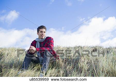 Young man sitting on grass View Large Photo Image Stock Photo - Young man sitting on grass. Fotosearch