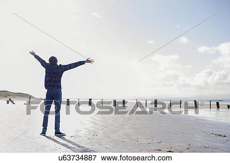 Stock Photo - Young man standing on beach with arms out, Brean Sands, Somerset, England. Fotosearch