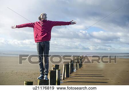 Stock Photo - Young man standing on groynes, Brean Sands, Somerset, England. Fotosearch