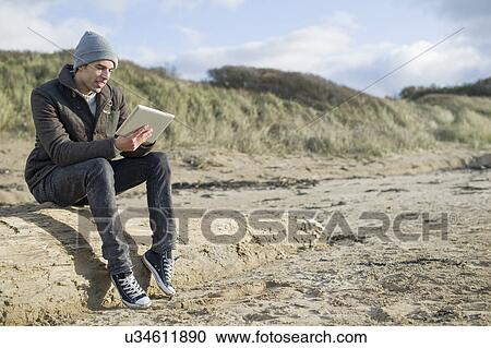 Young man using digital tablet, Brean Sands, Somerset, England View Large Photo Image Stock Image - Young man using digital tablet, Brean Sands, Somerset, England. Fotosearch