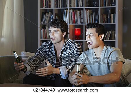 Young men shouting at tv, holding beer bottles View Large Photo Image Stock Photo - Young men shouting at tv, holding beer bottles. Fotosearch
