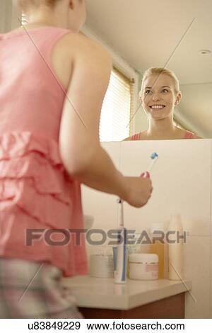 Stock Photo - Young woman in bathroom brushing teeth. Fotosearch