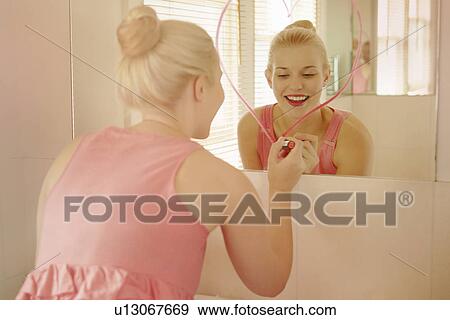 Stock Photo - Young woman in bathroom drawing heart shape on mirror with lipstick. Fotosearch
