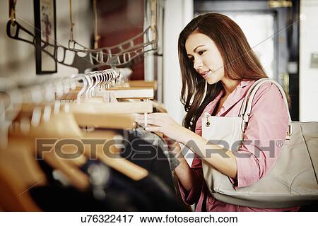 Young woman looking at selection of clothes on clothes rail View Large Photo Image Stock Photo - Young woman looking at selection of clothes on clothes rail. Fotosearch