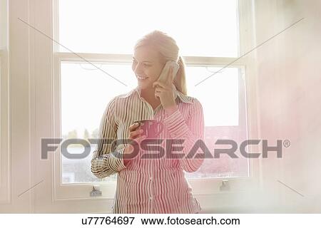 Stock Photo - Young woman on phonecall, holding hot drink. Fotosearch