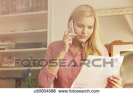 Stock Photograph - Young woman on telephone call, looking at paperwork. Fotosearch