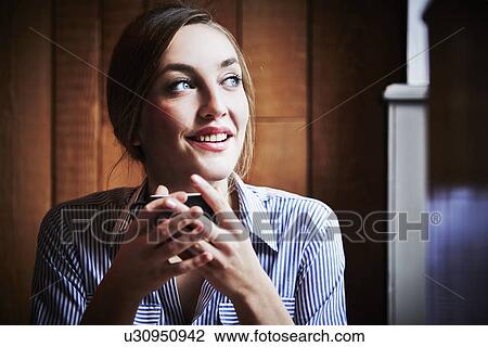 Young woman sitting in cafe holding hot drink View Large Photo Image Stock Image - Young woman sitting in cafe holding hot drink. Fotosearch