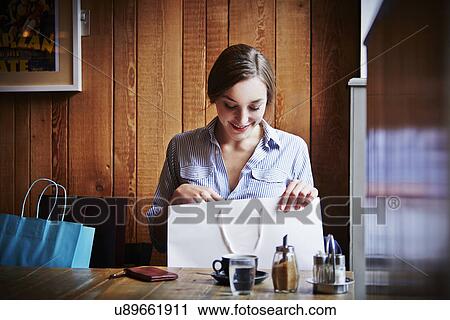 Young woman sitting in cafe looking in shopping bag View Large Photo Image Stock Image - Young woman sitting in cafe looking in shopping bag. Fotosearch