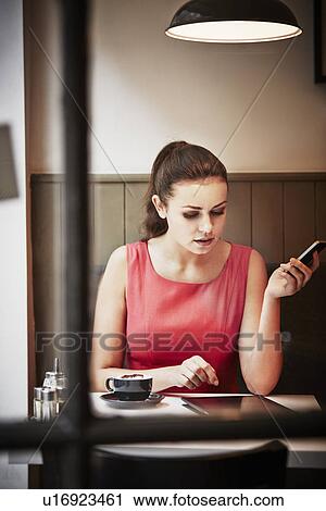 Young woman sitting in cafe with hot drink, digital tablet and smartphone View Large Photo Image Stock Image - Young woman sitting in cafe with hot drink, digital tablet and smartphone. Fotosearch