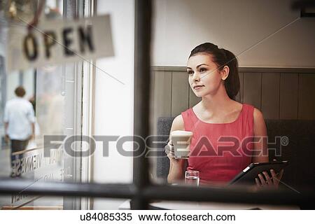 Stock Photography - Young woman sitting in cafe with digital tablet and hot drink. Fotosearch
