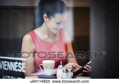 Stock Photography - Young woman sitting in cafe with digital tablet and hot drink. Fotosearch