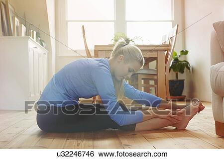Young woman sitting on floor leaning forwards touching toes View Large Photo Image Stock Photograph - Young woman sitting on floor leaning forwards touching toes. Fotosearch