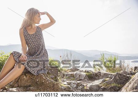 Young woman sitting on rocks shielding eyes View Large Photo Image Stock Image - Young woman sitting on rocks shielding eyes. Fotosearch