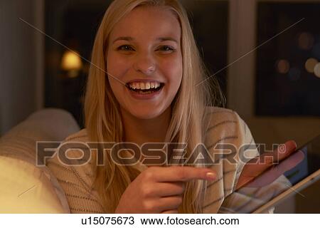 Young woman sitting on sofa, using digital tablet View Large Photo Image Stock Image - Young woman sitting on sofa, using digital tablet. Fotosearch
