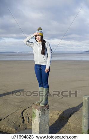 Stock Image - Young woman standing on groynes, Brean Sands, Somerset, England. Fotosearch