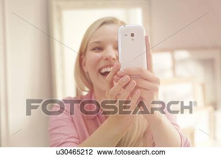 Stock Image - Young woman taking self portrait photograph using smartphone. Fotosearch