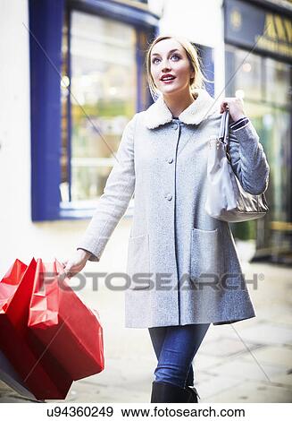 Stock Photo - Young woman walking down street carrying shopping bag. Fotosearch