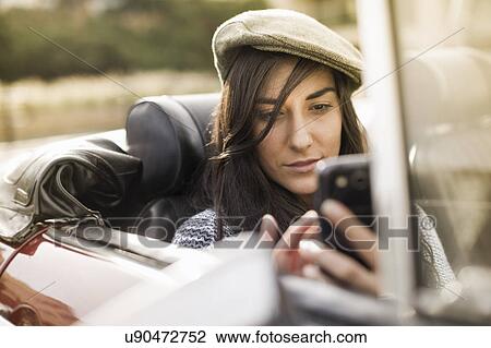 Young woman wearing flat cap in convertible using smartphone View Large Photo Image Stock Image - Young woman wearing flat cap in convertible using smartphone. Fotosearch