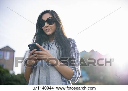 Picture - Young woman wearing sunglasses using smartphone. Fotosearch