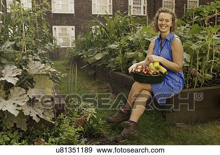 Stock Photo - Young woman with harvested vegetables on council estate allotment. Fotosearch