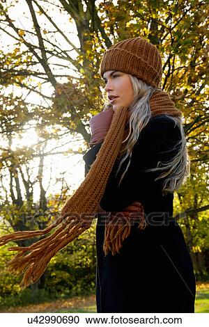 Stock Image - Young woman wrapped up in autumnal park. Fotosearch