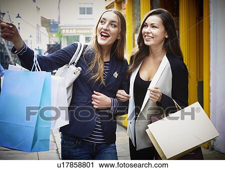 Young women arm in arm, carrying shopping bags down street View Large Photo Image Stock Image - Young women arm in arm, carrying shopping bags down street. Fotosearch