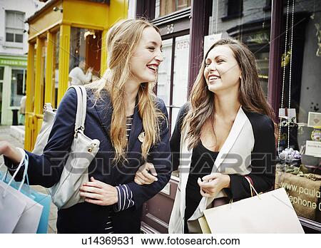 Young women walking down street carrying shopping bags and laughing View Large Photo Image Stock Image - Young women walking down street carrying shopping bags and laughing. Fotosearch
