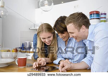 Stock Image - Youthful grandmother looking at digital with adult grandchildren. Fotosearch