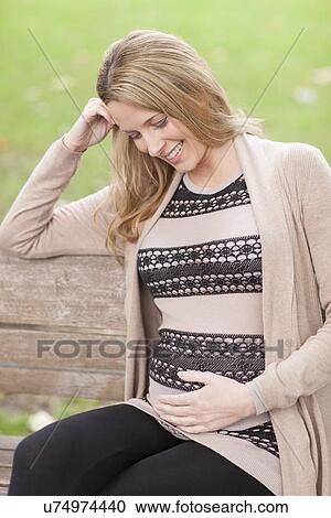 Stock Image - Pregnant woman sitting in park. Fotosearch