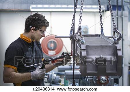 Picture - Apprentice engineer applying sealant to industrial gearbox in factory. Fotosearch
