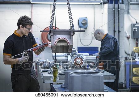 Stock Image - Apprentice engineer applying sealant to industrial gearbox in factory. Fotosearch